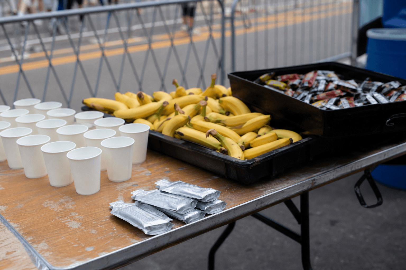 Marathon aid station table with unlabeled gels and bananas next to a runner’s own vegan packets, plantbaes.net